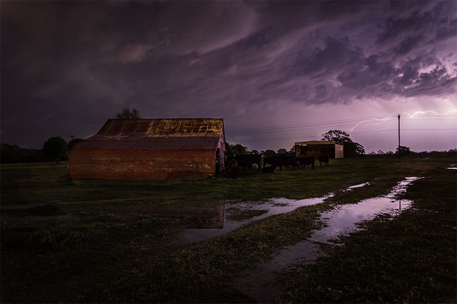 Photo of a farm with ominous clouds during a thunderstorm. A pole is stuck by lightning