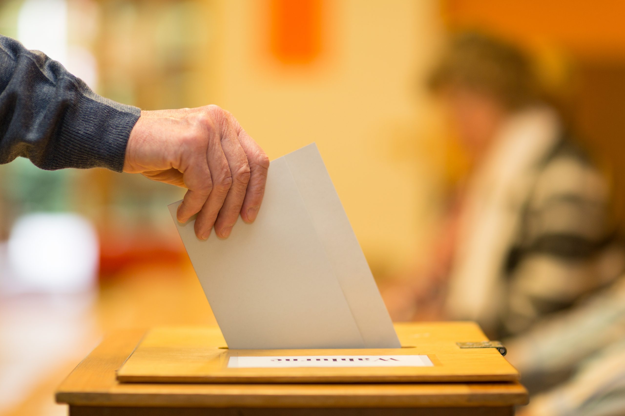 Image of man inserting ballot into a ballot box representing voting