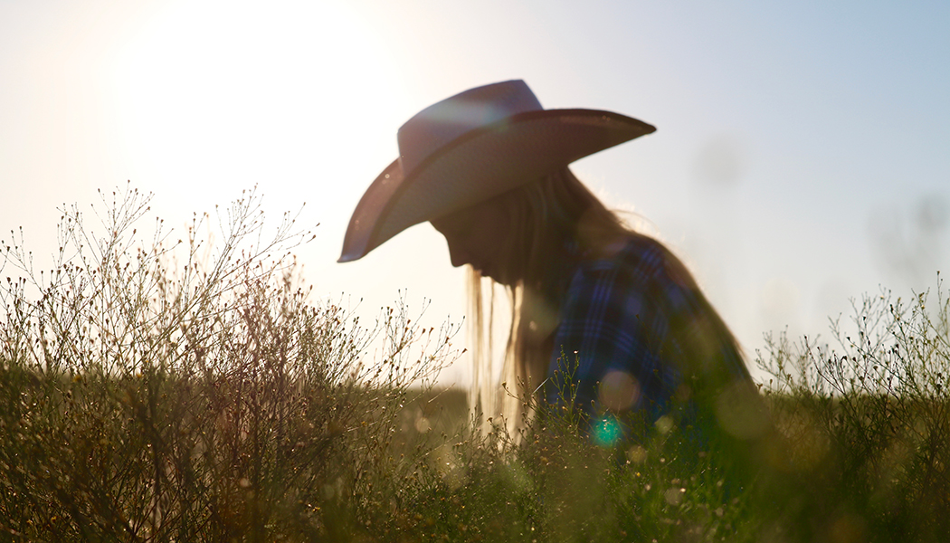 Woman in cowboy hat walking through fields