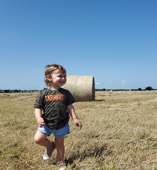 Smiling child walking in front of a hay bale on farm lands